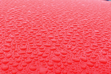 Hundreds and thousands of beaded water droplets on the surface of a waxed red car