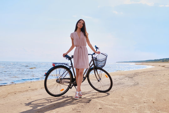 Young beautiful woman is enjoying summer with her bicycle at the seaside on the bright sunny day.