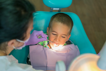 Obraz premium Pediatric dentist examining a little boys teeth in the dentists chair at the dental clinic. A child with a dentist in a dental office. Close up of dentist examination little boy's teeth in clinic