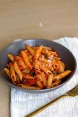 Sprinkling parmesan cheese on a plate of pasta with tomato sauce and eggplant. Selective focus.