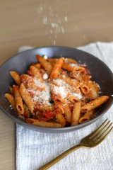 Sprinkling parmesan cheese on a plate of pasta with tomato sauce and eggplant. Selective focus.