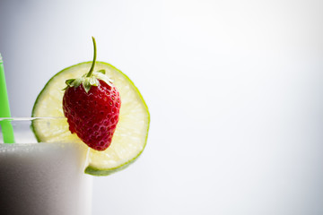 lime and ripe strawberries on a cocktail against white background
