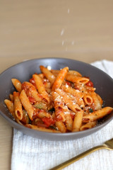 Sprinkling parmesan cheese on a plate of pasta with tomato sauce and eggplant. Selective focus.