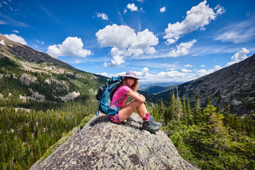 Fototapeta premium A young woman carrying a backpack, sitting on top of a mountain.
