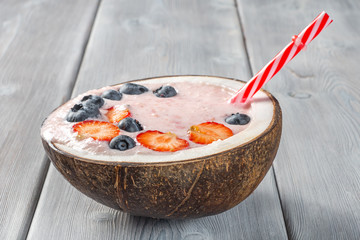 View of strawberry smoothie in a coconut bowl with blueberries on a white wooden background. Soft focus.