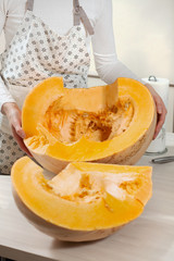 Kobieta prezentuje piękną pomarańczowa dynie która leży na kuchennym blacie w dwóch połówkach.