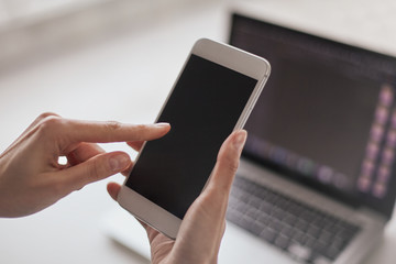 manos de mujer con celular y computadora fuera de foco de fondo.