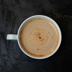 white cup with cappuccino and sweets on a stone black streaked table, top view, close-up, copy space