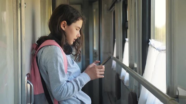 little girl walks on a train compartment car with a backpack and a smartphone. travel transportation railroad lifestyle concept. the girl in the train at the window corresponds the girl in the train