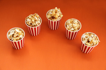 five striped red, white paper cups with popcorn on a bright orange background, close-up, copy space, fast food concept