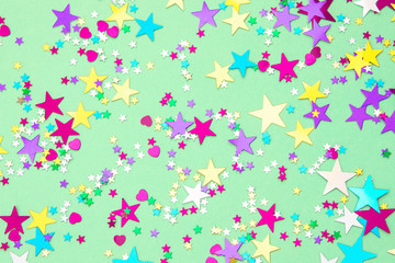 Colorful foil stars confetti sparse on trendy mint colored background. Simple holiday texture. Top view, flat lay