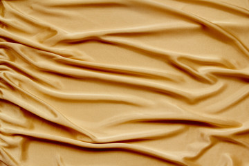 gold beautiful satin fabric draped with soft folds, silk cloth background, close-up, copy space