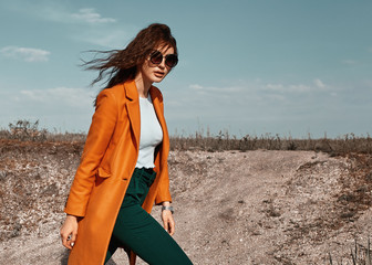 Autumn fashion. Beautiful attracrive young woman in bright autumn look. Orange trendy coat and pants and fashion sunglasses.