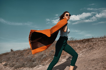 Autumn fashion. Beautiful attracrive young woman in bright autumn look. Orange trendy coat and pants and fashion sunglasses. - obrazy, fototapety, plakaty