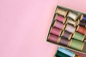 Colorful sewing threads lie in a box in a row gradient on a green background, selective focus. There is a place for text.