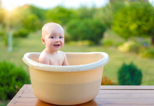 Baby bathes in a bath in the garden on a summer evening.