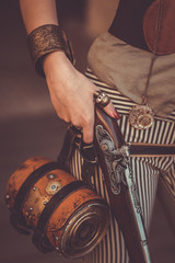 Close up of steampunk woman holding vintage pistol over striped costume.
