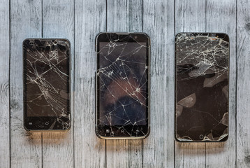 Set of three broken black mobile phones of different sizes, ready to repair their screens, on a gray surface
