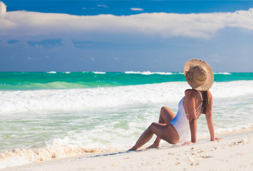 Young woman in bikini and straw hat relaxing at white caribbean beach