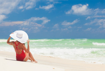 Fototapeta na wymiar Young woman in bikini and white straw hat relaxing at white caribbean beach