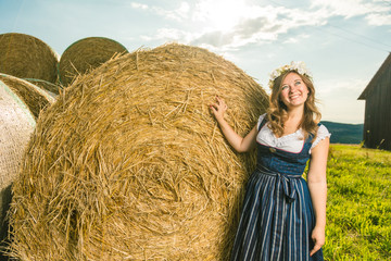 Frau in Tracht vor einem Strohballen an einem sonnigem Tag in bayern