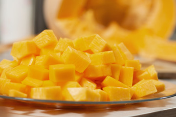 Kawałki świeżej dyni pokrojone w kostkę leżą na szklanym talerzu.