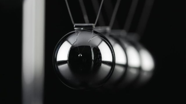 The chrome balls of a Newton&rsquo;s Cradle colliding in slow motion