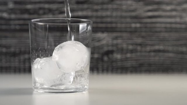 Clear water fills a glass cup with ice cubes. Slow motion. Black and white background