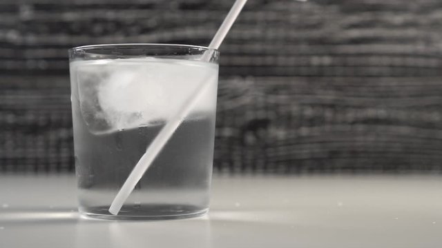 A white tubule spins in water with ice cubes in a glass cup. Slow motion. Black and white background