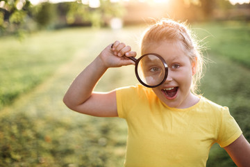 Outdoor portrait of young girl explores the outside world with magnifying glass in summer park. Childhood, positive emotions, summer concept