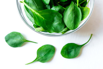 Fresh green spinach leaves in glass bowl on white table. Organic food, healthy diet, vegetarian...