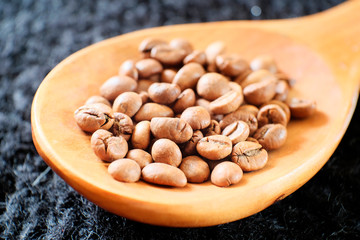 Coffee, Golden brown beans in a wooden spoon on a black grainy background. Shallow depth of field. Beautiful morning coffee beans