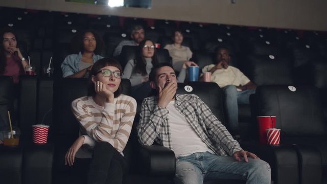 Guy is hugging pretty girl in cinema while she is resenting him taking hand off shoulder sitting back. Human feelings, emotions and relationship concept.