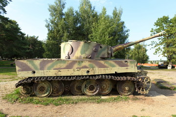 Old battle tank 2nd World War on the green grass under the trees.