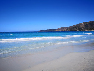 The blue clear water and white sand of a beach in Sardinia.