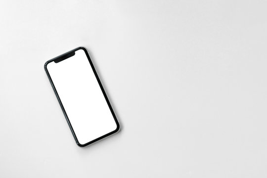 Smartphone lying on surface table or office desk. New modern black frameless smartphone mockup with white screen lying on surface. Isolated on white background.