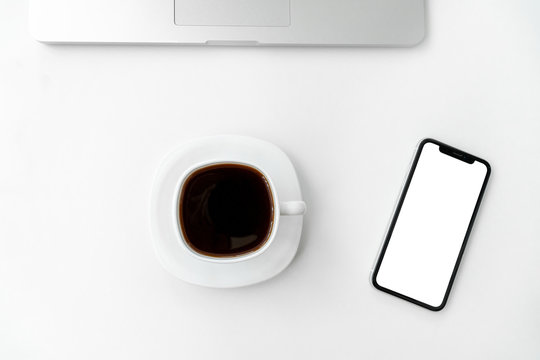 Mockup image of mobile phone with blank white screen, laptop and coffee cup with coffe on white background. Flat lay, top view modern minimalist blog header template.