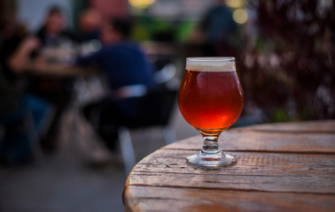 amber beer in tulip glass, craft beer on the patio, patio table with beer, patio lights, microbrewery, people in the background