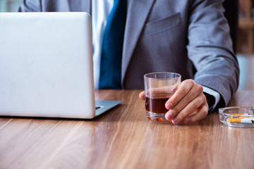 Male employee drinking alcohol and smoking cigarettes at workpla