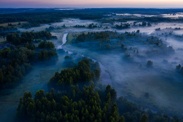 Aerial view of the forest, field and river covered with layers of thick morning fog