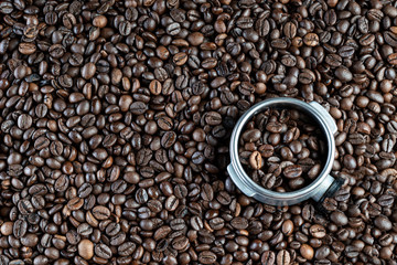 Background of roasted coffee beans and a professional coffee maker filter holder full of coffee. coffee maker filter holder