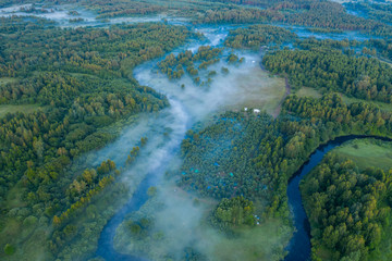 Aerial view of the forest, field and river covered with layers of thick morning fog