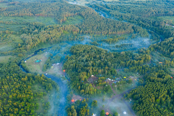 Aerial view of the forest, field and river covered with layers of thick morning fog