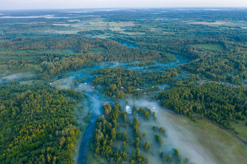 Fototapeta premium Aerial view of the forest, field and river covered with layers of thick morning fog
