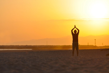 Fototapeta premium Silhouette of a Man on the beach meditating at sunset.