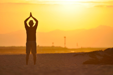Man meditating on the beach at sunset.