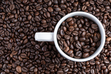 Background of roasted bean coffee with a white cup full of bean coffee on one side. full cup