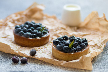 Tartalets with fresh berries on rumpled paper on a grey surface. 