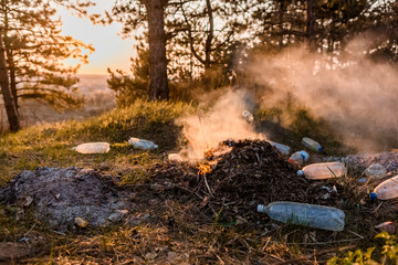 A pile of burning leaves next to a some plastic bottles in the forest.