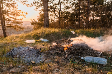 A heap of burning leaves next to a some bottles in the forest.